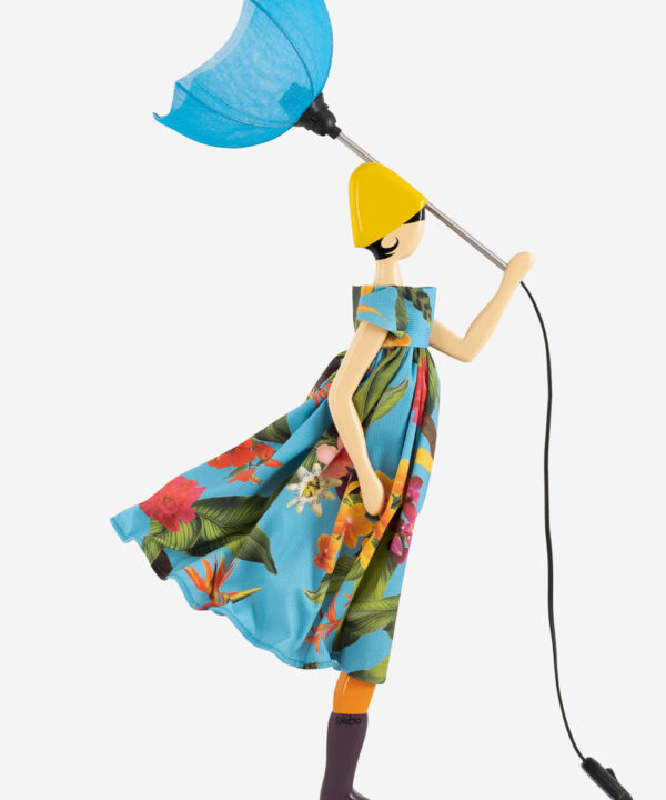 Designerlampe formet som en kvinde med en blå paraply iført en livlig blomsterkjole. Lampefiguren har en gul hat og en finurlig stil, der tilføjer et unikt og kunstnerisk præg til indretningen.