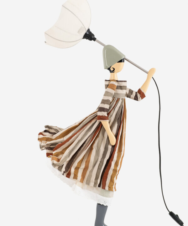 Unik designerlampe, der ligner en kvinde, der holder en hvid paraply, klædt i en flydende stribet kjole med jordfarver. Lampefiguren bærer en grå hat, der fremkalder en stilfuld og kreativ æstetik.